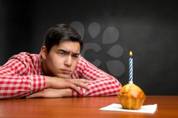 Sad birthday boy and a small cupcake with candle at the table