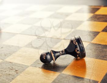Old black pawn lying on the chess board