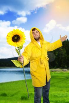 Man in yellow bathrobe holding a sunflower outdoor