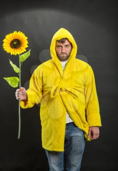 Man in yellow bathrobe holding a sunflower
