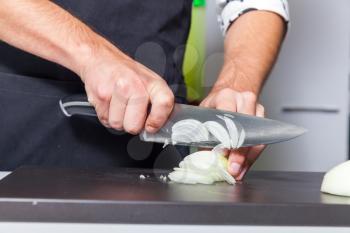 Close up of man's hands slicing onion on the board