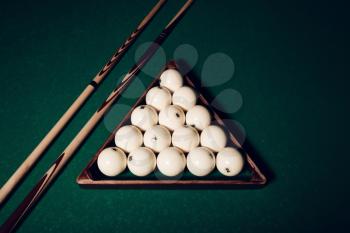 Billiard balls in wooden triangle and pool sticks close up view