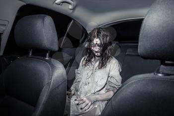 The horror zombie woman with bloody face in the car, night city on the background. Scary. Halloween.