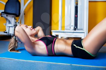 Young happy girl exercising abs in the gym