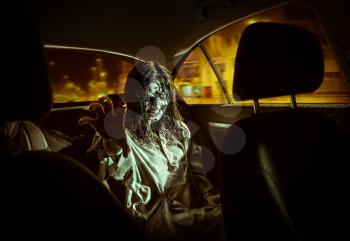 The horror zombie woman with bloody face in the car, night city on the background.