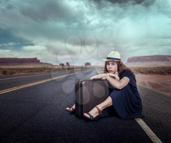 Young girl with luggage traveling hitchhiking. Rocky mountains on the background. Travel concept in retro style.