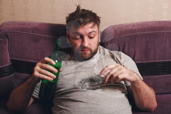 Hangover after hard drinking. Alcohol addicted man smoke cigarette with bottle in hand.