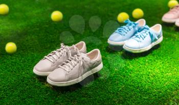 Few pairs of color sport shoes and yellow tennis balls on green grass with sunlight rays. 