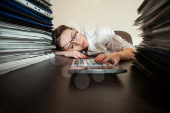 Tired female bookkeeper asleep against big stacks of documents and calculator