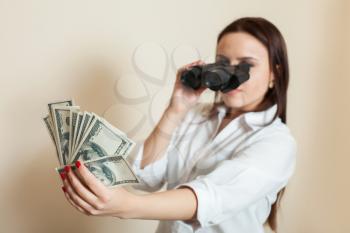 Young woman looks through binoculars on money fan. Success business lady concept