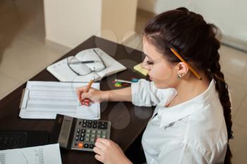 Young female bookkeeper considers on the calculator, top view on workplace with chancellery.