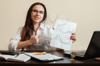 Young female accountant shows thumbs up after calculation