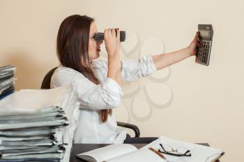 Young female accountant looks through binoculars on calculator