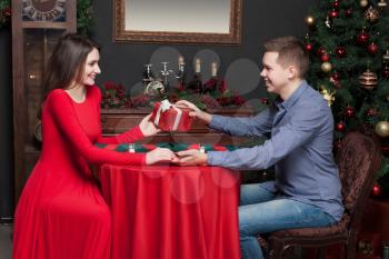 Smiling young man gives an attractive gift to beautiful woman. Rich interior of the luxury restaurant on background. Romantic date