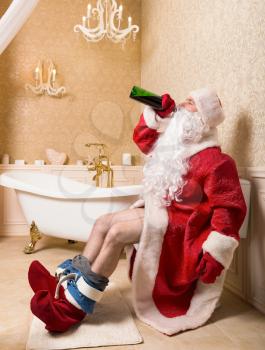 Drunk Santa Claus with bottle of alcohol sitting on the toilet. Christmas humor