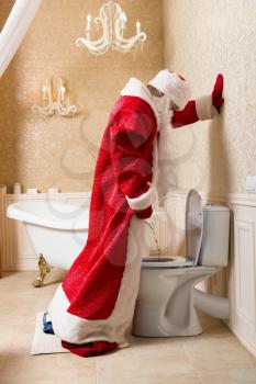 Funny drunk Santa Claus in red costume peeing in the toilet. Father Christmas alcoholic
