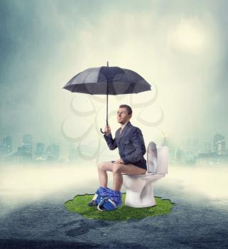 Man sitting on toilet bowl and holding umbrella in hands. Fog and the city skyline on background