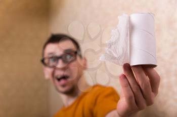 Surprised man in glasses sitting on the toilet bowl, out of paper