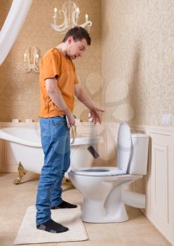 Man drops cell phone in toilet while peeing. Luxury bathroom interior on background