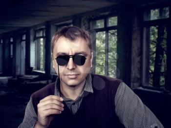 Young male with funny sunglasses on a stick, abandoned house on background. Fun photo props and accessories for photo shoots
