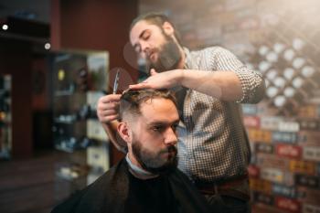 Coiffeur cutting by scissors hair of the customer man in black salon cape, barbershop on background