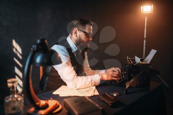 Portrait of bearded literature author in glasses typing on vintage typewriter. Creative people concept