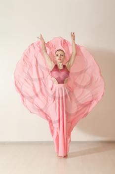 Young girl dancing in beautiful pink dress, back view. Professional dancer exercising in dance studio