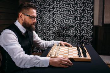Male player in glasses sitting against the chess board with the pieces set. Strategy game concept