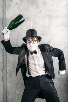 Mime actor with big bottle of alcohol performing a drunk man. Comedy pantomime artist in suit, gloves, glasses, make-up mask and hat