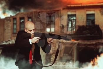 Killer in suit and red tie shoot a machine gun, night urban landscape with destroyed buildings on background. Contract murderer wallpaper or poster concept