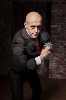 Bald contract killer in suit and red tie holds asterisk ninja. Professional secret agent explore oriental martial arts concept