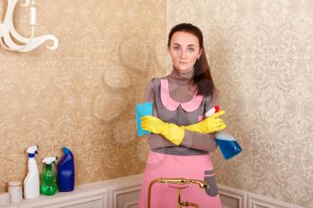 Woman in uniform and rubber gloves holding cleaning agent in hands. Housekeeping concept
