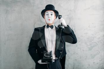 Pantomime theater actor with makeup mask performing with retro telephone. Comedy artist in suit, gloves and hat