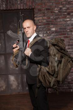 Contract killer ready for secret mission. Hired murderer in suit and red tie with backpack holding machine gun in hand. Brave professional agent