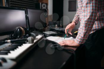 Male sound engineer hands on the table, musical keyboard, microphone and headphones on background. Digital music record studio. Media engineering