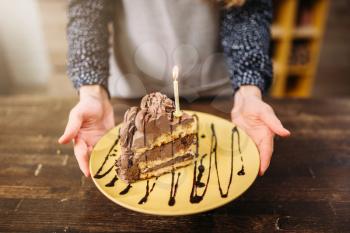 Male person hands holds plate with piece of cake decorated with candle and chocolate sauce, culinary masterpiece. Homemade cooking dessert