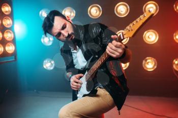 Male solo musican with electro guitar on the stage with the decorations of lights. Music entertainment. Bearded guitarist performing
