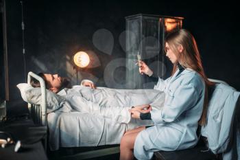 Female doctor with syringe against male patient in hospital bed. Illness of man in clinic, health recovery and treatment
