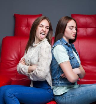 Two quarreling girls sits on red leather couch. End of female friendship. Women quarrel