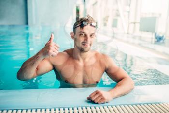 Muscular swimmer shows thumbs up in indoor swimming pool. Aqua sports exercise