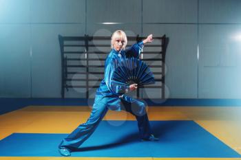 Female wushu master exercise with fan, martial arts. Woman in blue cloth on fight training