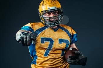 American football offensive player with ball pointing his finger at the camera, national league, black background. Contact sport