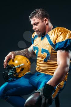 American football player with ball and helmet in hands, national league, black background