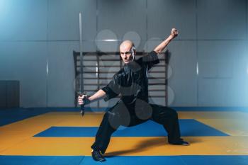 Wushu fighter with sword in action, martial arts. Man in black  cloth poses with blade