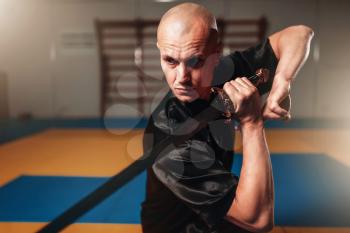 Male wushu master with blade in action, martial arts. Man in black  cloth poses with sword
