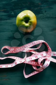 Apple and pink measuring tape on wooden table closeup. Weight loss diet concept, fat or calories burning