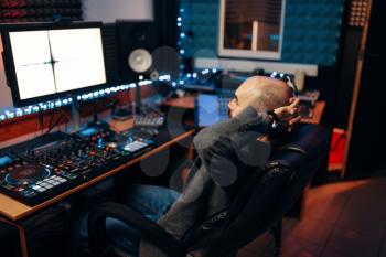 Male sound engineer at remote control panel, back view, recording studio. Musician at the mixer, professional audio processing