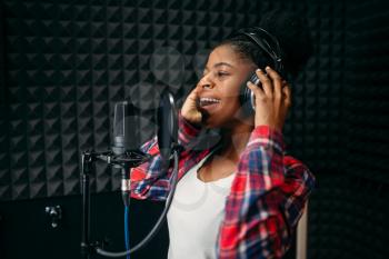 Female singer in headphones songs in audio recording studio. Musician  listens composition, professional music mixing
