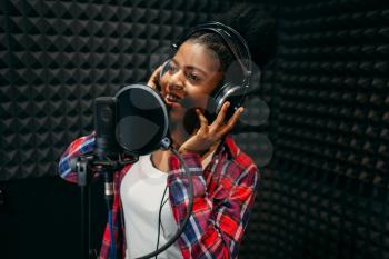 Female performer in headphones songs in audio recording studio. Musician listens composition, professional music mixing