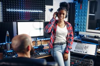 Sound producer and female performer in headphones listens composition in recording studio. Professional audio and music mixing technology
